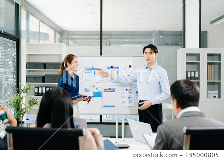 Asian business team presenting charts and reports in modern office meeting, showcasing teamwork, communication, and corporate strategy Asian business team presenting charts and reports in modern office meeting, showcasing teamwork, communication, and corporate strategy 135000805