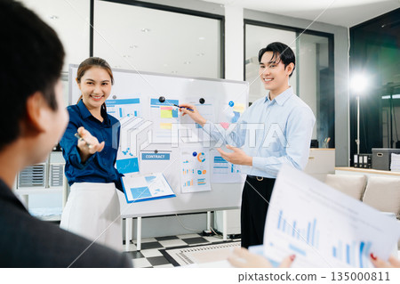 Smiling Asian business team shaking hands after successful meeting, symbolizing partnership, teamwork, and corporate success in a modern office 135000811