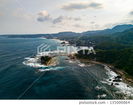 Ryugujima Island in Shimoda, Izu, and the red torii gate of Shirashima Shrine. Drone shot from Ogasaki Wing. Blue sea, white waves, and green forest. Ryugujima Island in Shimoda, Izu, and the red torii gate of Shirashima Shrine. Drone shot from Ogasaki Wing. Blue sea, white waves, and green forest. 135000864