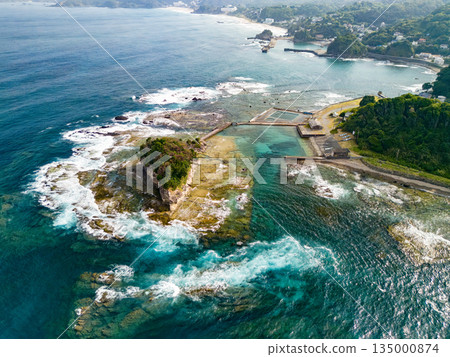 Ryugujima Island in Shimoda, Izu, and the red torii gate of Shirashima Shrine. Drone shot from Ogasaki Wing. Blue sea, white waves, and green forest. Ryugujima Island in Shimoda, Izu, and the red torii gate of Shirashima Shrine. Drone shot from Ogasaki Wing. Blue sea, white waves, and green forest. 135000874