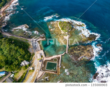Ryugujima Island in Shimoda, Izu, and the red torii gate of Shirashima Shrine. Drone shot from Ogasaki Wing. Blue sea, white waves, and green forest. Ryugujima Island in Shimoda, Izu, and the red torii gate of Shirashima Shrine. Drone shot from Ogasaki Wing. Blue sea, white waves, and green forest. 135000903