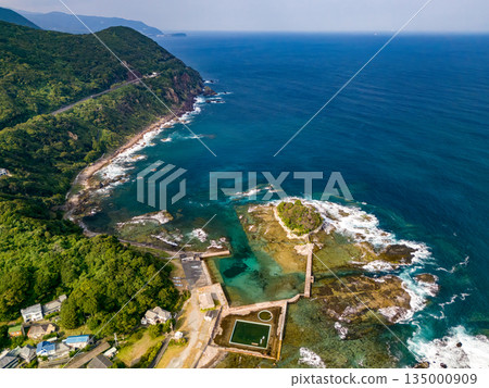 Ryugujima Island in Shimoda, Izu, and the red torii gate of Shirashima Shrine. Drone shot from Ogasaki Wing. Blue sea, white waves, and green forest. Ryugujima Island in Shimoda, Izu, and the red torii gate of Shirashima Shrine. Drone shot from Ogasaki Wing. Blue sea, white waves, and green forest. 135000909