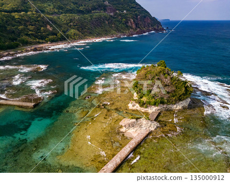 Ryugujima Island in Shimoda, Izu, and the red torii gate of Shirashima Shrine. Drone shot from Ogasaki Wing. Blue sea, white waves, and green forest. Ryugujima Island in Shimoda, Izu, and the red torii gate of Shirashima Shrine. Drone shot from Ogasaki Wing. Blue sea, white waves, and green forest. 135000912