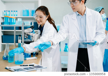 scientists conducting research investigations in a medical laboratory, a researcher in the foreground is using a microscope in laboratory for medicine. 135000958