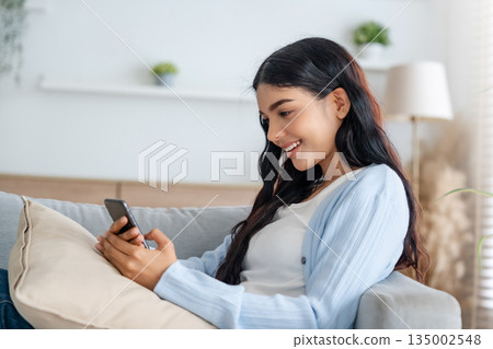 Smiling pretty young Asian woman sitting on cozy couch 135002548