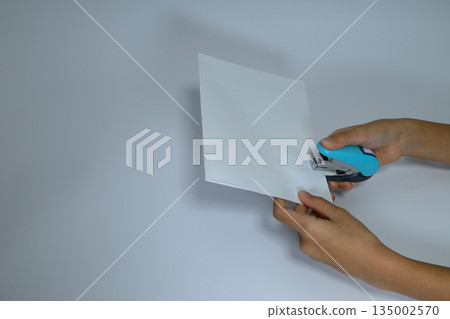 孩子的手正在用訂書機把白紙訂在一起。 孩子的手正在用訂書機把白紙訂在一起。 135002570