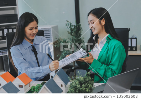 Professional real estate agents brainstorming house project while planning home investment with architectural model and documents 135002608