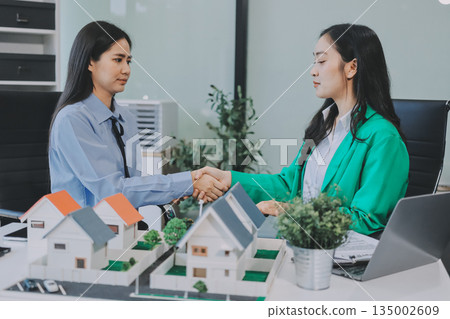 Professional real estate agents brainstorming house project while planning home investment with architectural model and documents 135002609