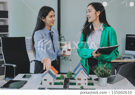 Professional real estate agents brainstorming house project while planning home investment with architectural model and documents 135002610