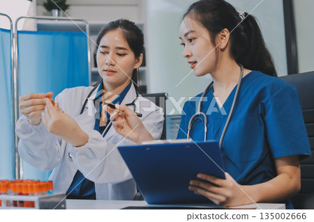 Medical team meeting analyzing blood test results in hospital laboratory. Doctors and scientists in lab coats are having a discussion about blood test result, holding test tubes and taking notes. 135002666