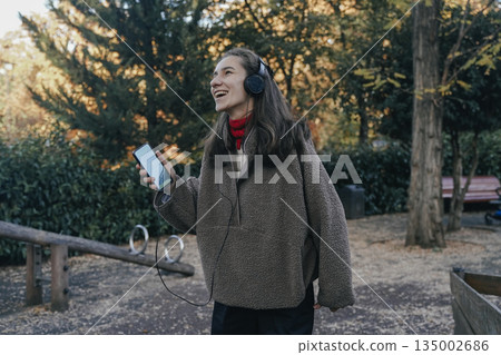 Peaceful Woman Relaxing and Listening to Music in Autumn Park Peaceful Woman Relaxing and Listening to Music in Autumn Park 135002686
