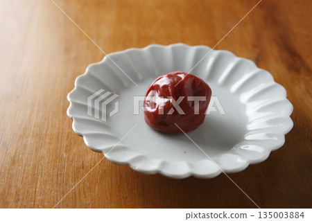 盤子上放著一顆醃梅子，背景是木紋。 135003884