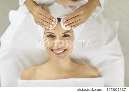 Portrait of happy beautiful young woman getting facial treatment at beauty salon 135003887