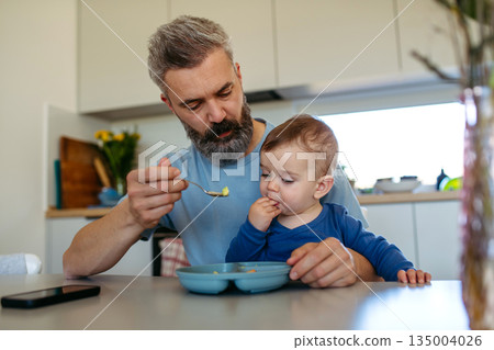 Caring father feeding toddler during mealtime at home. Caring father feeding toddler during mealtime at home. 135004026