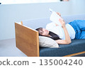Young Japanese woman reading a book on the sofa 135004240