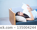 Young Japanese woman reading a book on the sofa 135004244