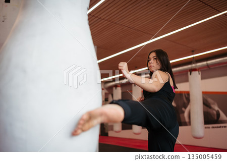 Woman training kickboxing on punching bag in gym. 135005459