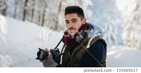 Male photographer holding camera during winter walk in snowy nature. Male photographer holding camera during winter walk in snowy nature. 135005617