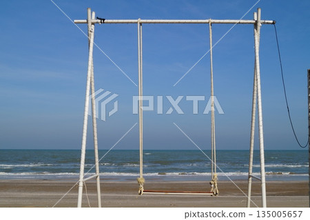A beautiful place on the stone seashore with a swing against the backdrop of a blue sky and turquoise sea. A beautiful place on the stone seashore with a swing against the backdrop of a blue sky and turquoise sea. 135005657
