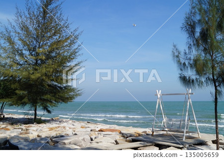 A cozy place on the seashore.A beautiful place on the stone seashore with a swing against the backdrop of a blue sky and turquoise sea. 135005659