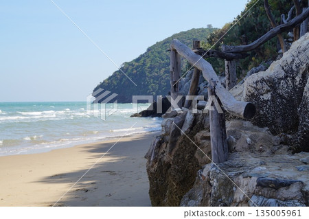Stone stairs on the beach.A stone staircase with wooden handrails leads up the mountain. Against the backdrop of a blue sky and turquoise sea. Stone stairs on the beach.A stone staircase with wooden handrails leads up the mountain. Against the backdrop of a blue sky and turquoise sea. 135005961