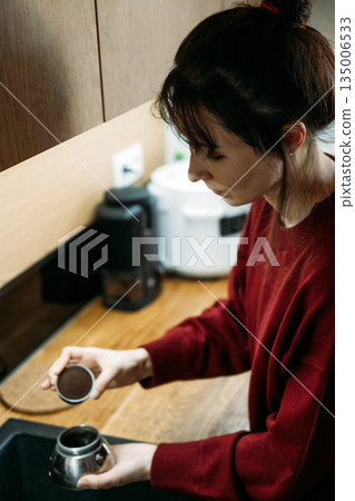 Young woman prepares moka pot by placing filter basket into base at kitchen sink. Coffee brewing workflow, manual brewing process, professional coffee preparation. Young woman prepares moka pot by placing filter basket into base at kitchen sink. Coffee brewing workflow, manual brewing process, professional coffee preparation. 135006533
