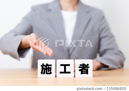 A middle-aged female business woman wearing a suit with a construction worker's block 135006820