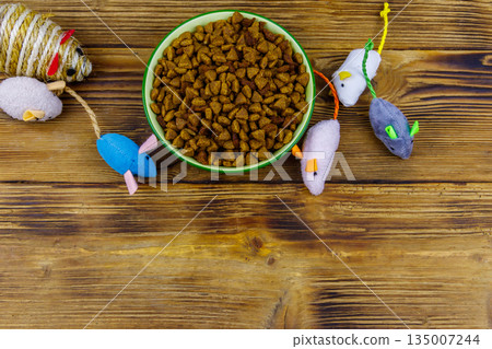 Set of mouses toys for cat and bowl with dry pet food on wooden background. Top view, copy space. Pet care concept Set of mouses toys for cat and bowl with dry pet food on wooden background. Top view, copy space. Pet care concept 135007244