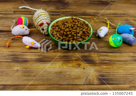 Set of toys for cat and bowl with dry pet food on wooden background. Pet care concept Set of toys for cat and bowl with dry pet food on wooden background. Pet care concept 135007245