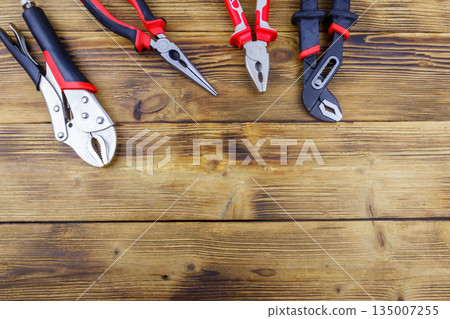 Set of different pliers on wooden background. Top view, copy space Set of different pliers on wooden background. Top view, copy space 135007255