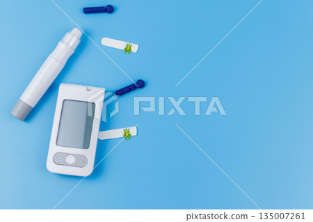 Digital glucometer, lancet pen, disposable needles and test strips on pastel blue background. Top view, copy space. Diabetes concept Digital glucometer, lancet pen, disposable needles and test strips on pastel blue background. Top view, copy space. Diabetes concept 135007261