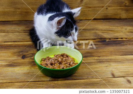 Kitten eating his food from ceramic bowl on wooden floor 135007321