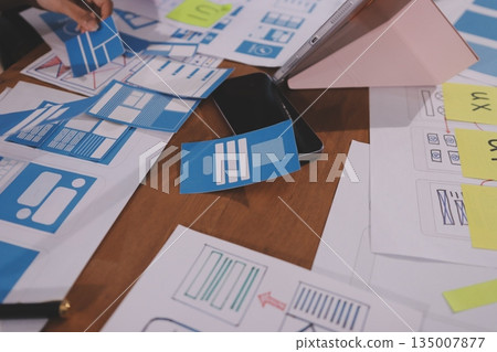 Close up ux developer and ui designer brainstorming about mobile app interface wireframe design on table with customer breif and color code at modern office.Creative digital development agency. Close up ux developer and ui designer brainstorming about mobile app interface wireframe design on table with customer breif and color code at modern office.Creative digital development agency. 135007877