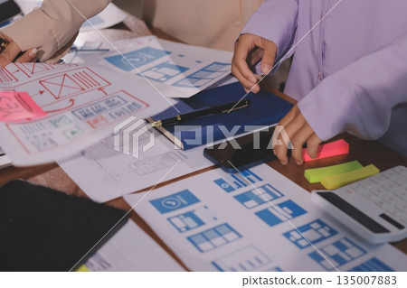 Close up ux developer and ui designer brainstorming about mobile app interface wireframe design on table with customer breif and color code at modern office.Creative digital development agency. Close up ux developer and ui designer brainstorming about mobile app interface wireframe design on table with customer breif and color code at modern office.Creative digital development agency. 135007883
