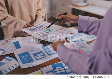 Close up ux developer and ui designer brainstorming about mobile app interface wireframe design on table with customer breif and color code at modern office.Creative digital development agency. 135007893
