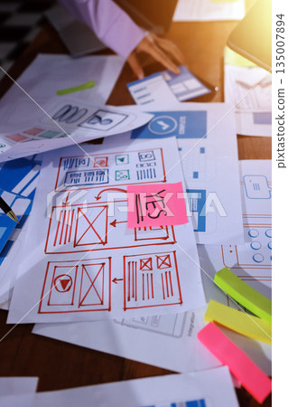 Close up ux developer and ui designer brainstorming about mobile app interface wireframe design on table with customer breif and color code at modern office.Creative digital development agency. 135007894