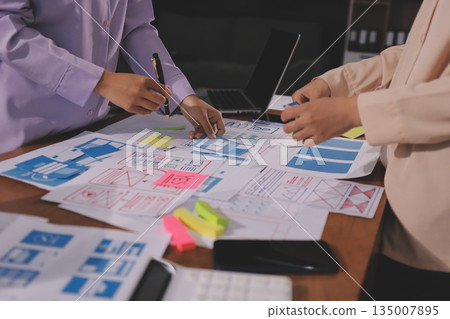 Close up ux developer and ui designer brainstorming about mobile app interface wireframe design on table with customer breif and color code at modern office.Creative digital development agency. Close up ux developer and ui designer brainstorming about mobile app interface wireframe design on table with customer breif and color code at modern office.Creative digital development agency. 135007895