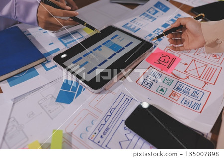 Close up ux developer and ui designer brainstorming about mobile app interface wireframe design on table with customer breif and color code at modern office.Creative digital development agency. Close up ux developer and ui designer brainstorming about mobile app interface wireframe design on table with customer breif and color code at modern office.Creative digital development agency. 135007898