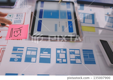 Close up ux developer and ui designer brainstorming about mobile app interface wireframe design on table with customer breif and color code at modern office.Creative digital development agency. Close up ux developer and ui designer brainstorming about mobile app interface wireframe design on table with customer breif and color code at modern office.Creative digital development agency. 135007900