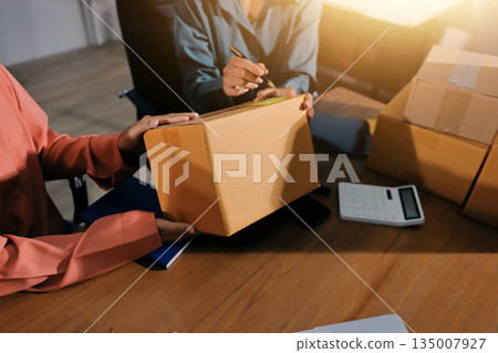 Startup SME small business entrepreneur of freelance Asian woman wearing apron using laptop and box to receive and review orders online to prepare to pack sell to customers, online sme business ideas. 135007927