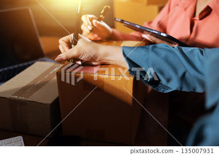 Startup SME small business entrepreneur of freelance Asian woman wearing apron using laptop and box to receive and review orders online to prepare to pack sell to customers, online sme business ideas. 135007931