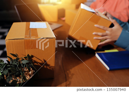 Startup SME small business entrepreneur of freelance Asian woman wearing apron using laptop and box to receive and review orders online to prepare to pack sell to customers, online sme business ideas. 135007940