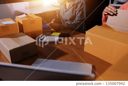 Startup SME small business entrepreneur of freelance Asian woman wearing apron using laptop and box to receive and review orders online to prepare to pack sell to customers, online sme business ideas. Startup SME small business entrepreneur of freelance Asian woman wearing apron using laptop and box to receive and review orders online to prepare to pack sell to customers, online sme business ideas. 135007942