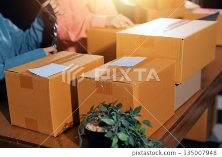 Startup SME small business entrepreneur of freelance Asian woman wearing apron using laptop and box to receive and review orders online to prepare to pack sell to customers, online sme business ideas. Startup SME small business entrepreneur of freelance Asian woman wearing apron using laptop and box to receive and review orders online to prepare to pack sell to customers, online sme business ideas. 135007948