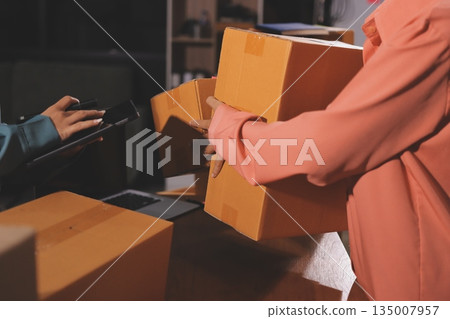 Startup SME small business entrepreneur of freelance Asian woman wearing apron using laptop and box to receive and review orders online to prepare to pack sell to customers, online sme business ideas. Startup SME small business entrepreneur of freelance Asian woman wearing apron using laptop and box to receive and review orders online to prepare to pack sell to customers, online sme business ideas. 135007957