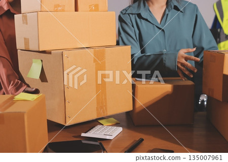 Startup SME small business entrepreneur of freelance Asian woman wearing apron using laptop and box to receive and review orders online to prepare to pack sell to customers, online sme business ideas. 135007961