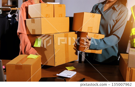 Startup SME small business entrepreneur of freelance Asian woman wearing apron using laptop and box to receive and review orders online to prepare to pack sell to customers, online sme business ideas. 135007962