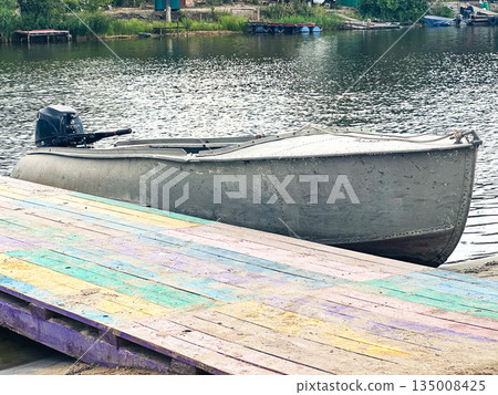 A rustic motorboat on a colorful dock by a calm lake. 135008425