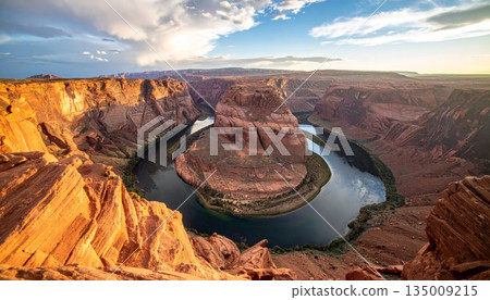 A breathtaking sunset illuminates the red rock cliffs and desert landscape of Grand Canyon National Park in Arizona, offering a grand view of the valley and mountains under a cloudy sky 135009215