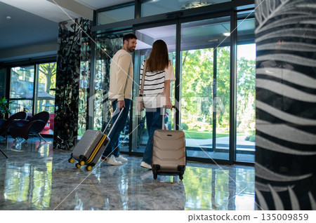 Cute couple with suitcases in the luxury hotel lobby Cute couple with suitcases in the luxury hotel lobby 135009859